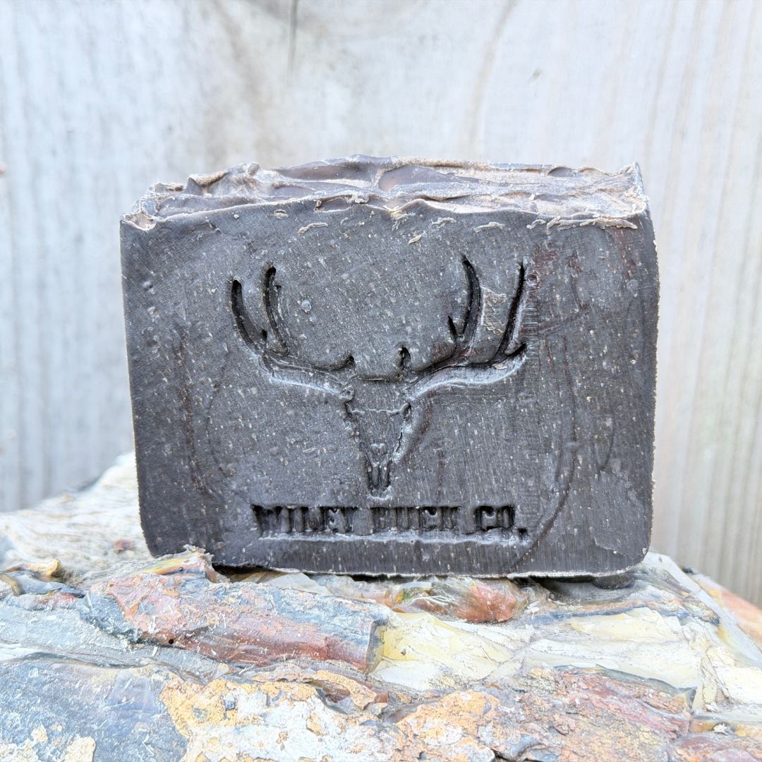 Bar of soap with a deer skull design and 'Wiley Buck Co.' branding on a stone surface.