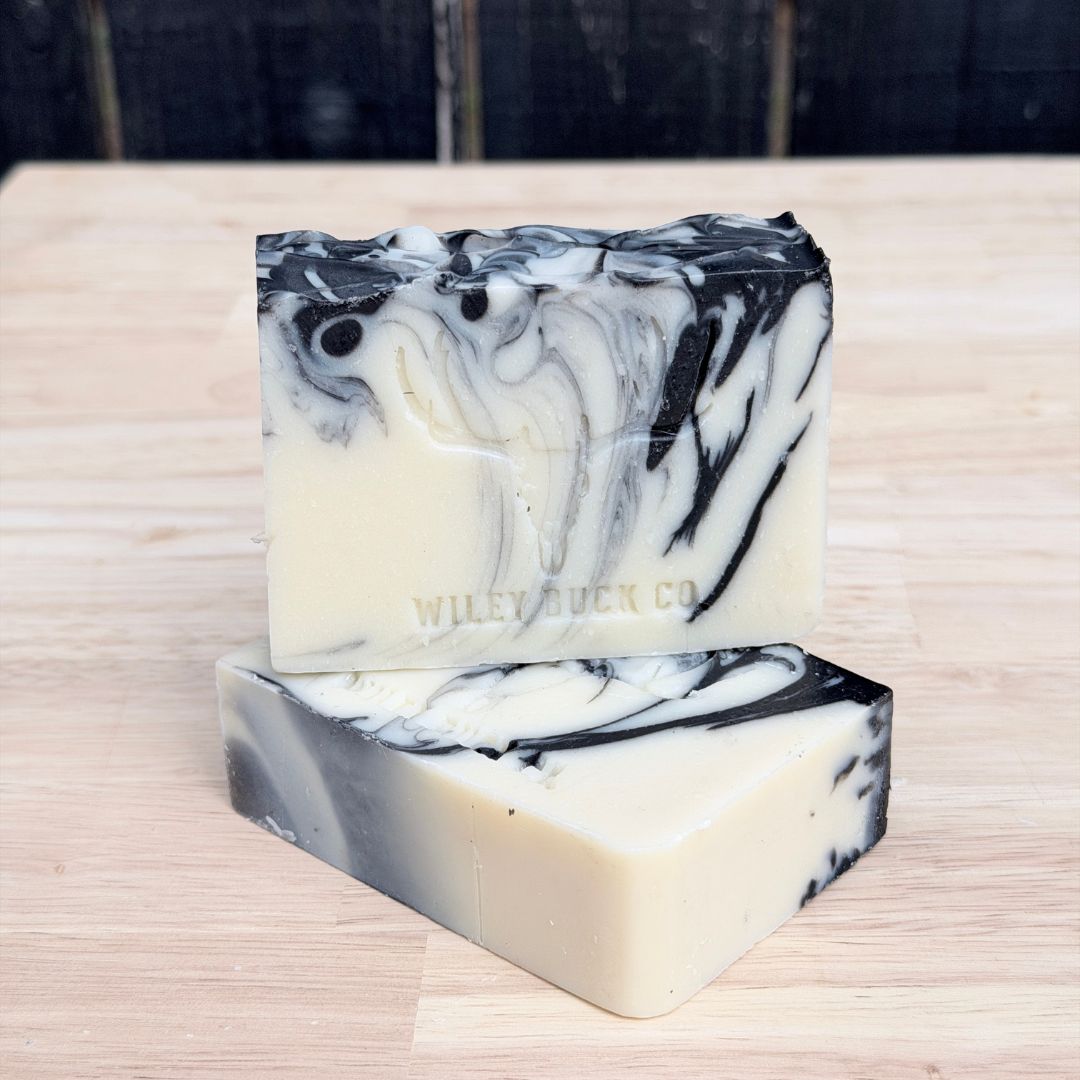 Two marbled black and white soap bars on a wooden surface with 'Wiley Buck Co' branding.