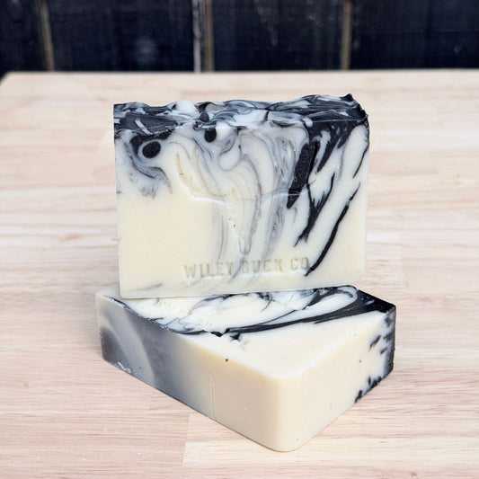 Two marbled black and white soap bars on a wooden surface with 'Wiley Buck Co' branding.
