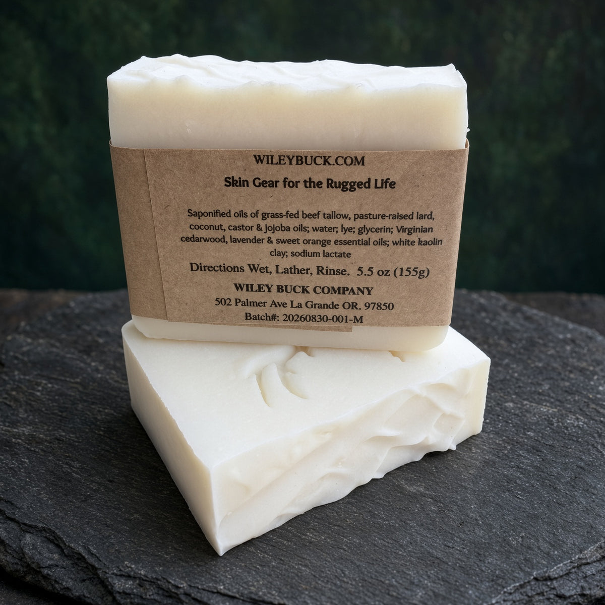 Two rectangular bars of off-white soap stacked on a dark slate surface, with a kraft paper label wrapped around the top bar. The label reads WILEYBUCK.