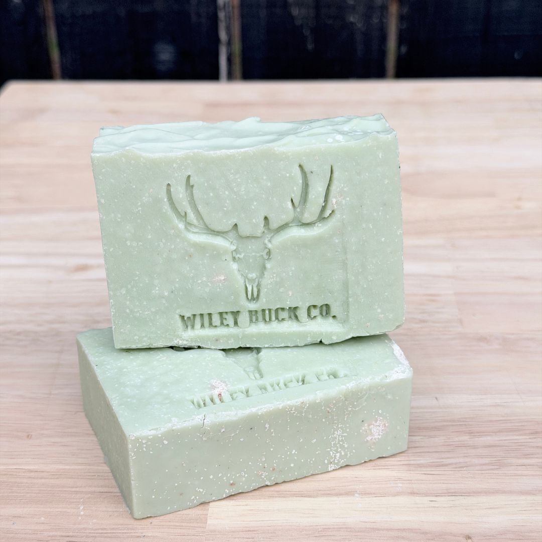 Two green soap bars with a deer emblem and 'Wiley Buck Co.' text on a wooden surface.