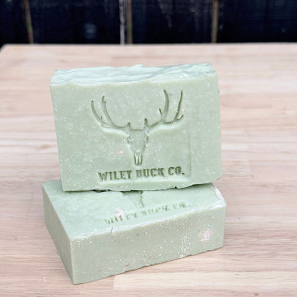 Two green soap bars with a deer emblem and 'Wiley Buck Co.' text on a wooden surface.