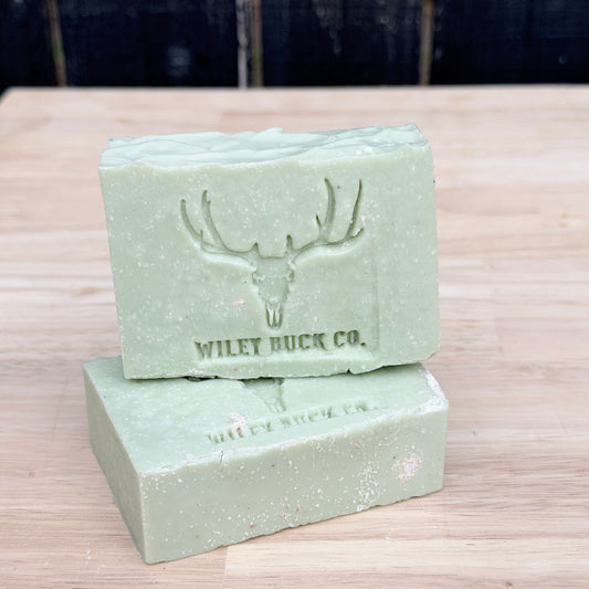 Two green soap bars with a deer emblem and 'Wiley Buck Co.' text on a wooden surface.