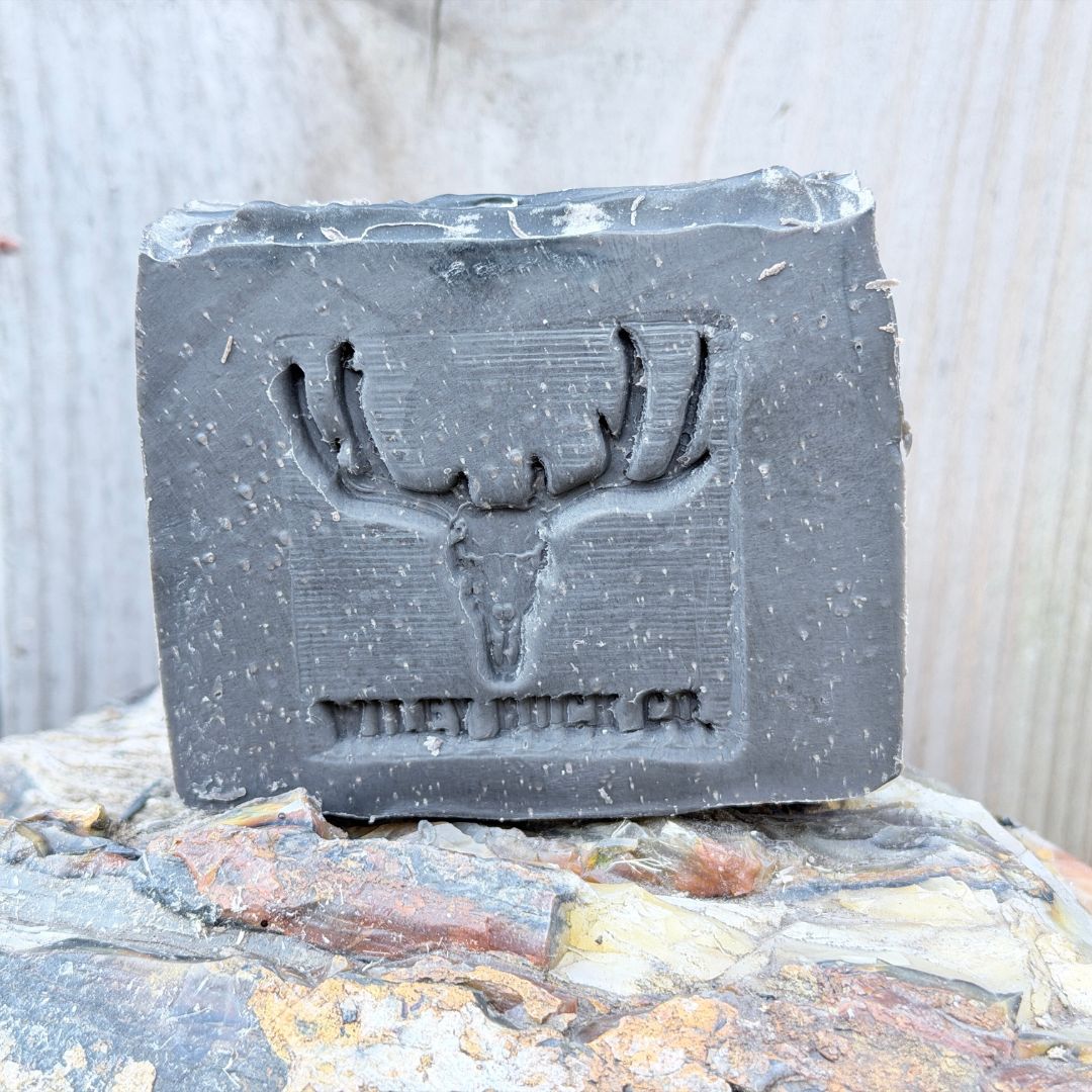 Bar of soap with a deer skull design and 'Wiley Buck Co.' branding on a stone surface.