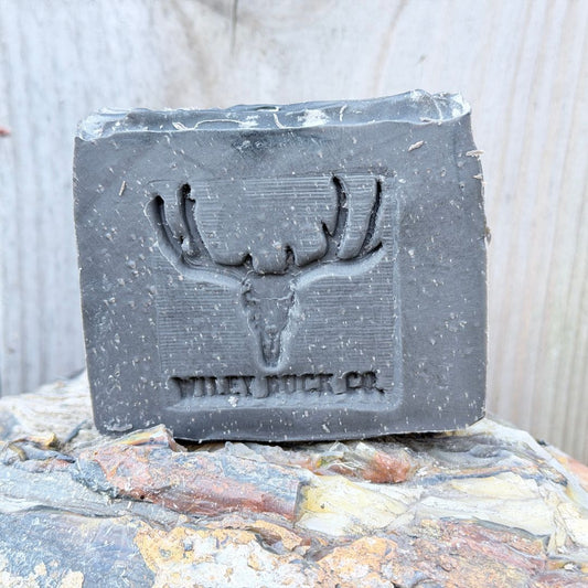 Bar of soap with a deer skull design and 'Wiley Buck Co.' branding on a stone surface.