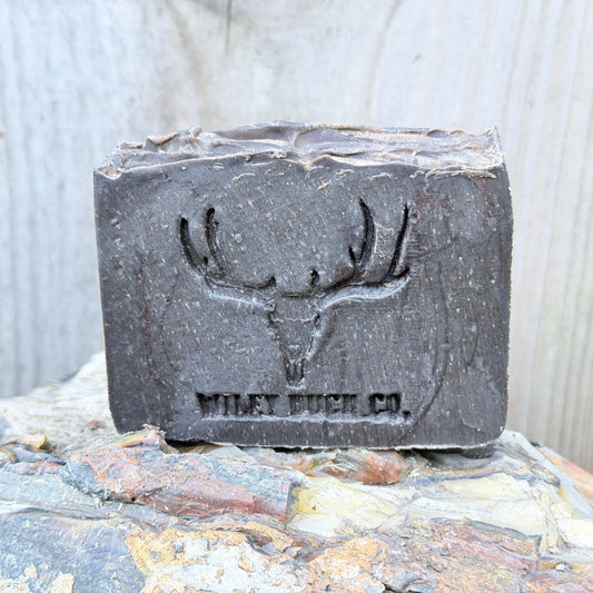 Bar of soap with a deer skull design and 'Wiley Buck Co.' branding on a stone surface.