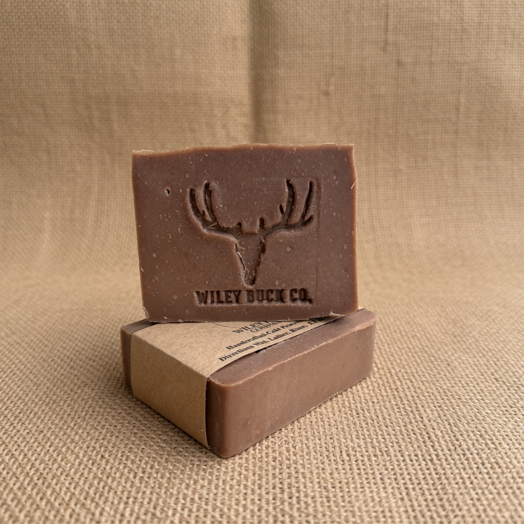 A rectangular bar of brown soap standing upright on top of its kraft paper box, with the soap embossed deer head logo and the brand name 'WILEY BUCK CO.' visible.