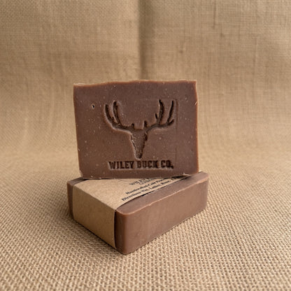 A rectangular bar of brown soap standing upright on top of its kraft paper box, with the soap embossed deer head logo and the brand name 'WILEY BUCK CO.' visible.
