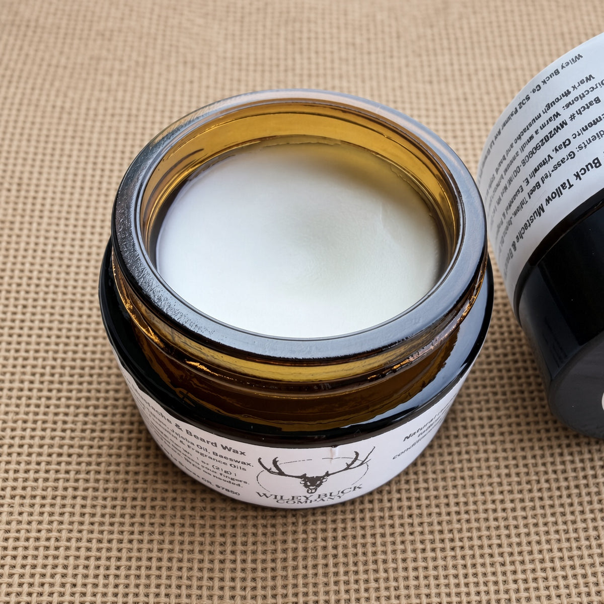 An open amber glass jar of Wiley Buck Mustache and Beard Wax on a burlap mat background