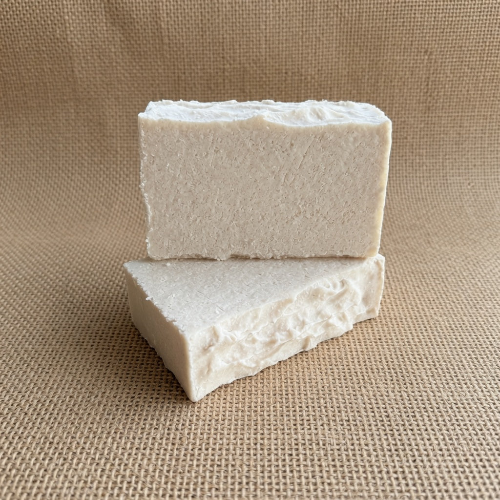 Two blocks of white soap stacked on a beige fabric background